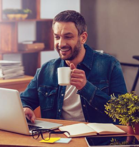 Inspiriert mit einer Tasse frischem Kaffee. Selbstbewusster junger Mann arbeitet am Laptop und hält eine Kaffeetasse, während er an seinem Arbeitsplatz im Büro sitzt.