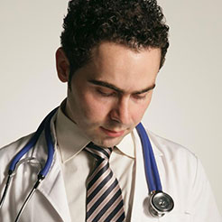 Ein Arzt in weissem Kittel und Krawatte mit Stethoskop betrachtet sein Mobiltelefon.