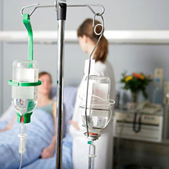 Zwei Infusionsgefässe im Vordergrund und verschwommen im Hintergrund eine Patientin und eine Ärztin im Gespräch