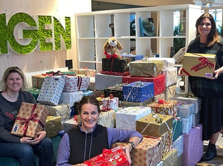 Drei Mitarbeiterinnen von Amgen in der Schweiz sitzen vor einem Berg mit Geschenken, die sie für bedürftige Kinder liebevoll eingepackt haben. 