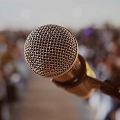 Im Vordergrund ein Mikrofon und im Hintergrund verschwommen Menschen.